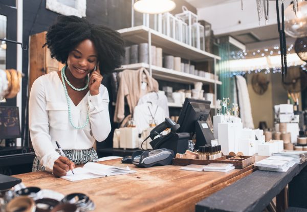 Shot of a happy young shopkeeper using her cellphone while standing behind the counter in her shop